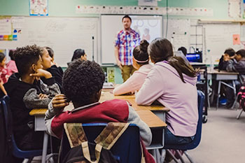 K-12 Students in a classroom with teacher in the front| Photo by Kenny Eliason on Unsplash
