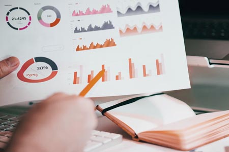 Photo of a hand holding a paper with some charts and a book on a desk